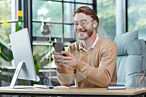 Young man businessman, freelancer sits in the office and uses the phone. Type messages, chstting