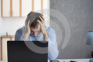 Young man businessman works with laptop and tiredly holds his hands on his head. Problems at work. Professional burnout photo