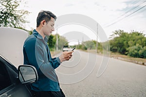 Young man calling,  texting for car service on roadside assistance after broken car. Car broken, car breakdown concept