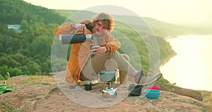 young man camper tourist pouring hot tea, going to drink coffee