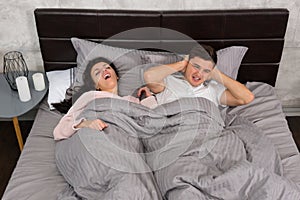 Young man can not sleep and covers his ears because his girlfriend snoring while sleeping