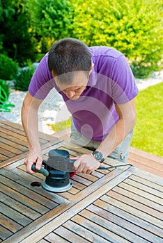 Young man - carpenter working with electric sander in the garden