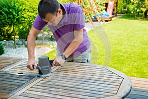 Young man - carpenter working with electric sander in the garden