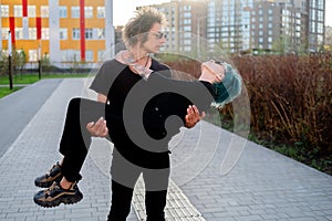 A young man carries his girlfriend in his arms. A couple dressed in black clothes on the street in the city