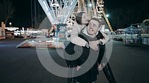 A young man is carrying a beautiful woman on his back. Date at the amusement park.