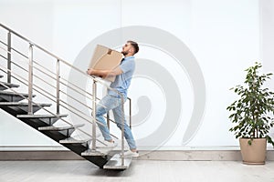 Young man carrying carton box upstairs indoors