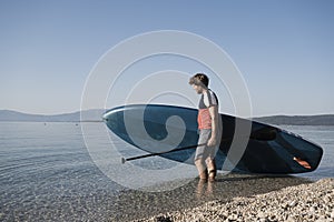 Young man carrying his stand up paddle board into the calm sea water
