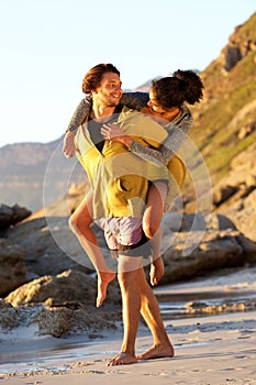 Young man carrying woman on his back at the beach