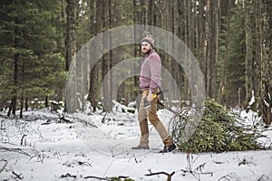 Young man is caryying christmas tree in the wood