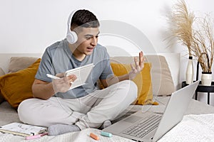 Young man with casual clothes sitting on the bed at home with laptop computer and studying. Man using e-learning