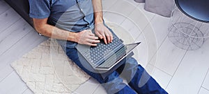 Young man in casual clothes sitting on floor and working on his laptop computer at home. Stay home and work online. Quarantine