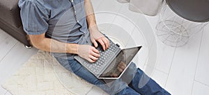 Young man in casual clothes sitting on floor and working on his laptop computer at home. Stay home and work online. Quarantine