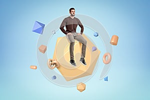 Young man in casual clothes sitting on geometric polygon with random objects on blue background