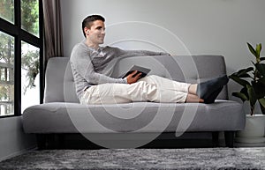 Young man in casual clothes sitting on sofa and using digital tablet