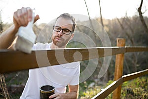 Young man in casual clothing painting wooden fence in his backyard