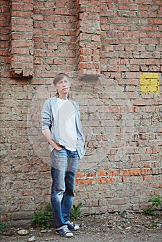 Young man  in casual clothing standing in full size near brick wall background