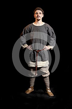 young man in casual gray clothes and a hat of the Viking Age looks serious, hands on hips