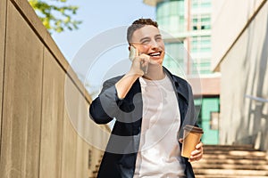 A young man in a casual outfit with a jacket, walking outdoors, talking on a mobile phone