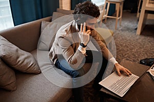 Young man in casual stylish clothes sitting on the sofa and surfing the net