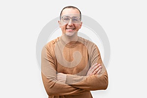 Young man in a casual sweater and glasses on a light background. Positive man with crossed arms looking at camera