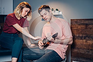 Young man in casual wear play ukulele, his girlfriend sit next to him