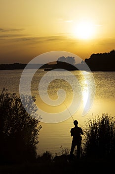 A young man catches fish in the lake at sunset. Beautiful sun reflection on the water. Relaxation