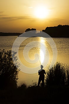 A young man catches fish in the lake at sunset. Beautiful sun reflection on the water. Relaxation