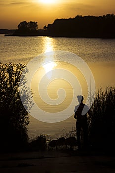 A young man catches fish in the lake at sunset. Beautiful sun reflection on the water. Relaxation