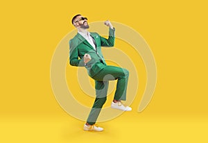 Happy excited man in green party suit celebrating success and dancing on yellow background