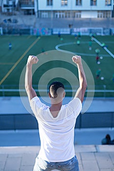 Young man celebrating victory on bleachers watching football