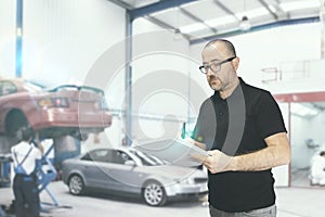 Young man with a check list for a car revision. Repair workshop with empty copy space