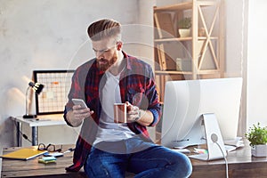 Young man in checkered shirt holding smartphone and cup of coffee