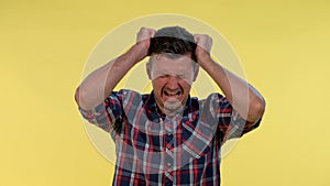 Young man in checkered shirt putting fists on head and screaming in pain