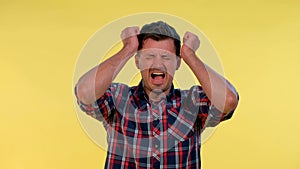 Young man in checkered shirt putting fists on head and screaming in pain