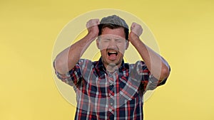 Young man in checkered shirt putting fists on head and screaming in pain