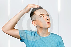 Young man checking hair in mirror, dressed in a blue t shirt