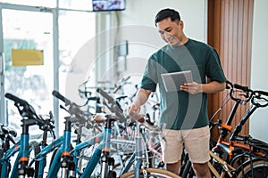young man checks the handlebars of a bicycle while using a tablet