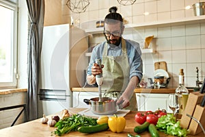 Young man, chef cook using hand blender while preparing Italian meal in the kitchen