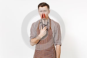 Young man chef in striped brown apron holding black kitchen serving plastic pair of tongs for salad on nose isolated on