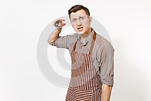 Young man chef in striped brown apron, shirt holding black kitchen serving plastic pair of tongs for salad isolated on