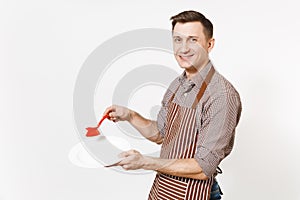 Young man chef in striped brown apron, shirt holds washes white round empty clear plate with red brush for washing