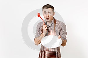 Young man chef in striped brown apron, shirt holds washes white round empty clear plate with red brush for washing