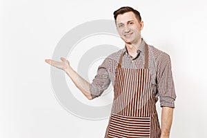 Young man chef or waiter pointing hand aside on copy space in striped brown apron, shirt isolated on white background