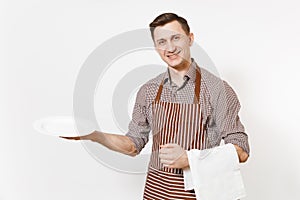 Young man chef or waiter in striped brown apron, shirt holding white round empty clear plate, towel napkin isolated on