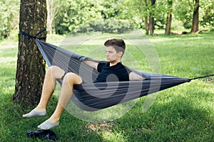 Young man chilling in hammock among trees. Social distancing. Small group of people enjoying conversation at picnic with social