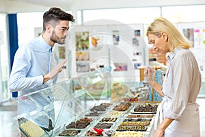 young man choosing luxury chocolates from confectioners counter