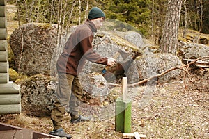 Young man chops wood with an ax in the forest. Guy chops a tree into logs with an cleaver in natura