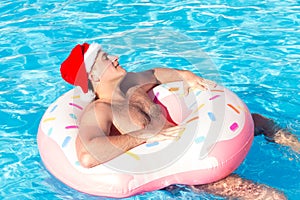 Young man in christmas hat is floating on inflatable air ring circle in pool with blue water