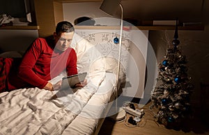 young man in christmas pyjama in bed watching a tablet