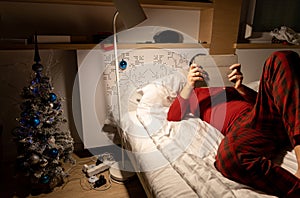 young man in christmas pyjama in bed watching a tablet